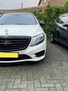 two cars parked next to each other in front of a brick wall and shrubbery