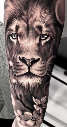 a black and white photo of a lion with flowers on it's leg tattoo