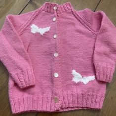 a pink cardigan with white birds on it sitting on top of a wooden floor