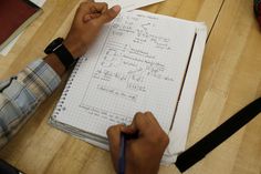 a person is writing on a notebook while sitting at a table with other papers and pens