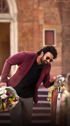 a man in sunglasses and a red jacket holding a bunch of flowers next to stairs