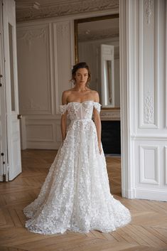 a woman in a wedding dress standing on a wooden floor with an open doorway behind her