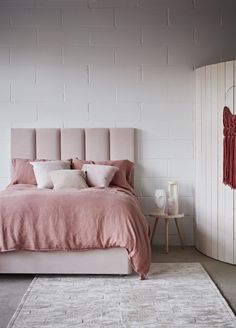 a bed with pink linens and pillows in a white room next to a brick wall