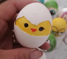 a hand holding an egg that has been painted to look like a chick's face