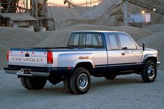 a silver chevrolet truck parked in front of a pile of dirt and gravel at dusk