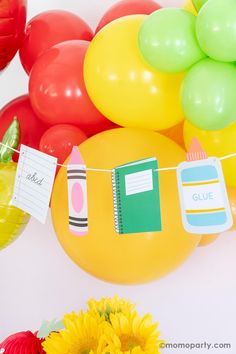 colorful balloons and flowers are hanging from a string with note cards attached to them on a white wall