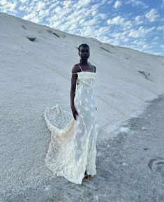 a woman in a white dress standing on top of a snow covered hill with her hands in her pockets