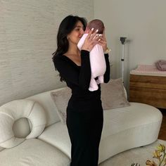 a woman in a black dress holding a pink baby doll and posing for the camera