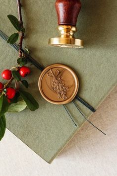 a wax stamp on top of a piece of paper next to some leaves and berries