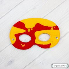 a red and yellow mask sitting on top of a white wooden floor with holes in it