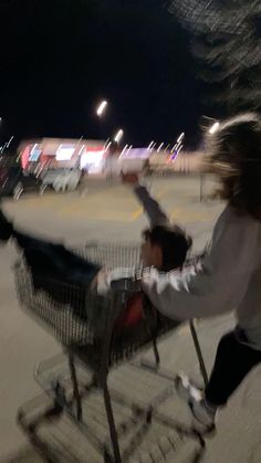 two children are pushing a shopping cart in the parking lot at night with their arms outstretched