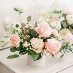 a white vase filled with pink and white flowers on top of a table next to a mirror