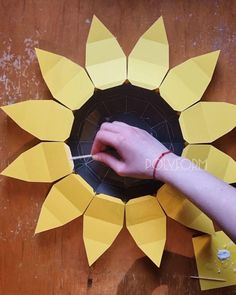 someone is making a paper sunflower out of construction paper and glues it on the wall