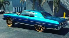 a blue car with gold rims parked in a parking lot next to palm trees