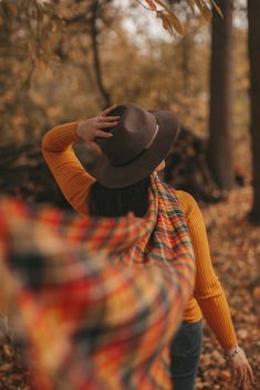 a woman wearing a hat and scarf walking through the woods with her hands on her head