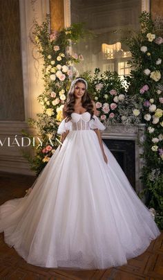 a woman in a white wedding dress standing next to a flowered wall and fireplace