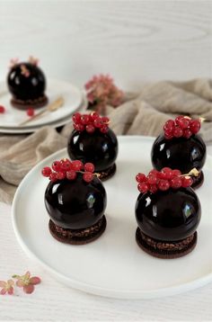 three chocolate desserts with red berries on top sit on a white plate next to flowers