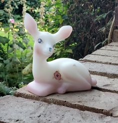 a small white rabbit sitting on top of a brick wall next to bushes and trees