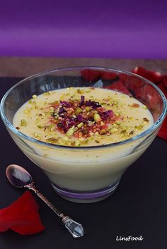 a dessert in a glass bowl with fruit and nuts on the rim next to a spoon