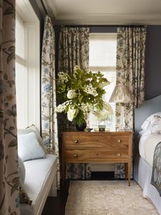 a bed room with a neatly made bed next to a window and a flower vase