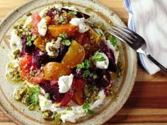 a white plate topped with lots of food on top of a wooden table next to a fork