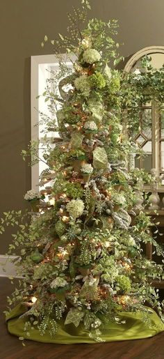 a decorated christmas tree in front of a mirror on a wooden floor with green and white decorations