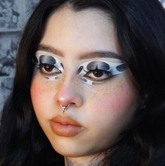 a woman with black hair and white makeup has fake eyelashes on her face while wearing silver eyeliners