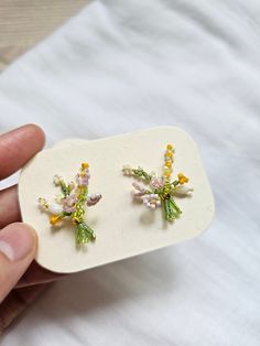 a person is holding two small earrings in their left hand and the other one has flowers on it