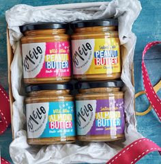 four jars of peanut butter in a box with ribbon on the table next to it