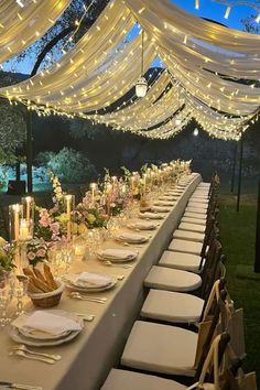 a long table is set up with white linens and candles for an elegant dinner