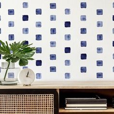 a vase with a plant on top of a wooden shelf in front of a blue and white wall