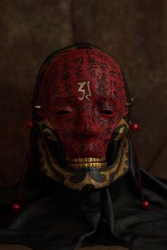 a red mask with writing on it is sitting in front of a brown wall and black cloth