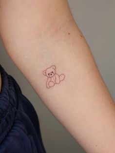 a small teddy bear tattoo on the left inner arm and wrist, with an outline of a teddy bear