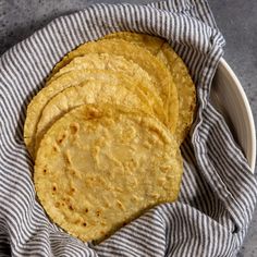 four corn tortillas in a bowl on top of a blue and white towel