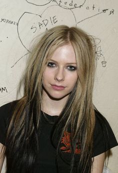 a young woman with long hair standing in front of a white wall and writing on the wall behind her