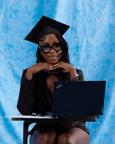 a woman sitting at a desk with a laptop in front of her, wearing a graduation cap and gown