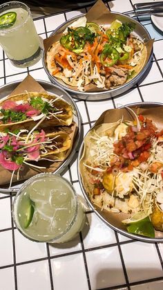 three plates of food sitting on top of a white tiled table next to glasses and drinks