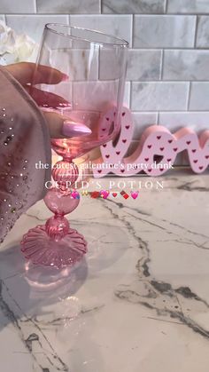 a person holding a wine glass with pink liquid in it on a marble counter top