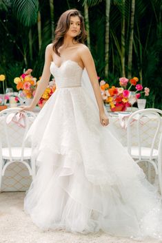 a woman in a wedding dress standing next to a table with chairs and flowers on it