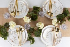 the table is set with white and gold plates, silver utensils, and flowers