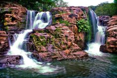 the waterfall is surrounded by large rocks and greenery