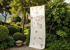 a white towel hanging from a clothes line in a garden with trees and bushes around it