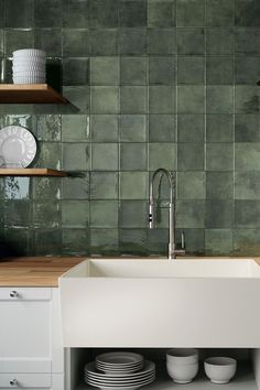 a kitchen with green tiles on the wall and white dishes in the bottom drawer under the sink