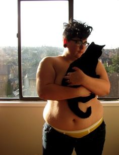 a woman holding a black cat in her belly while standing next to a large window