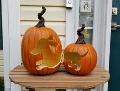 two pumpkins with dogs cut out of them on a wooden table in front of a house