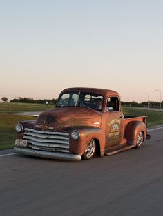 an old truck driving down the road with grass in the backgrouund and sky in the background