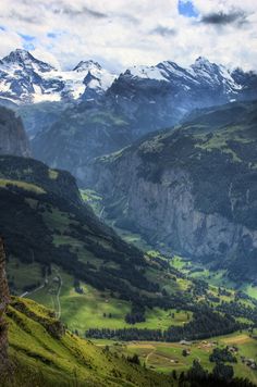 a mountain valley with snow capped mountains in the distance and green grass on both sides