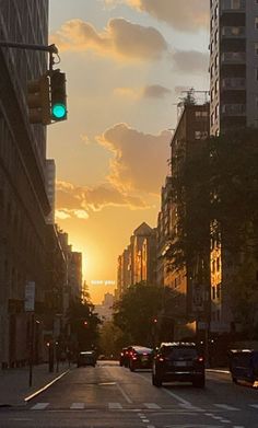 the sun is setting on an urban street with tall buildings and cars driving down it