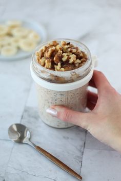 a hand holding a jar filled with granola and walnuts next to a spoon