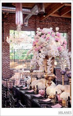 a tall vase filled with white and pink flowers on top of a long black table